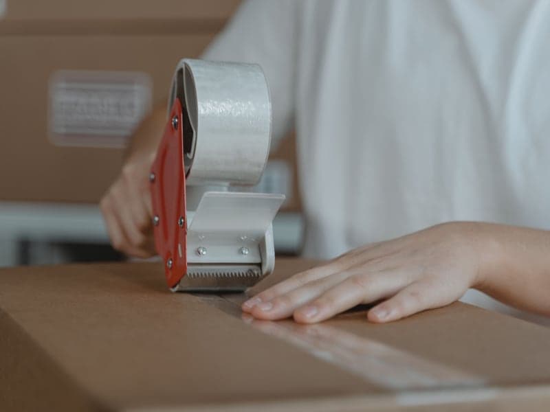 A person sealing a cardboard shipping box with tape